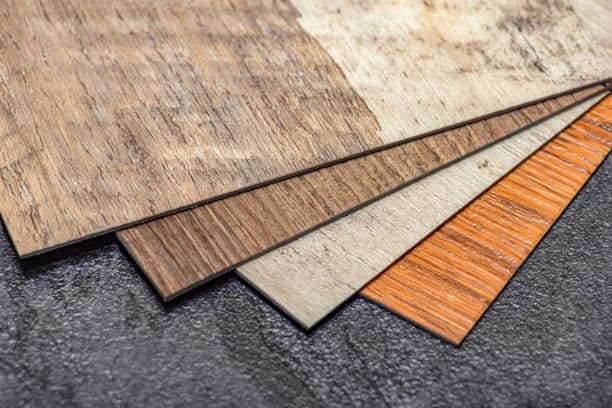 Four vinyl plank samples in different wood and stone finishes fanned out on a dark concrete surface